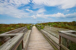 A wooden boardwalk leading through a natural landscape with grassy areas and a clear sky.