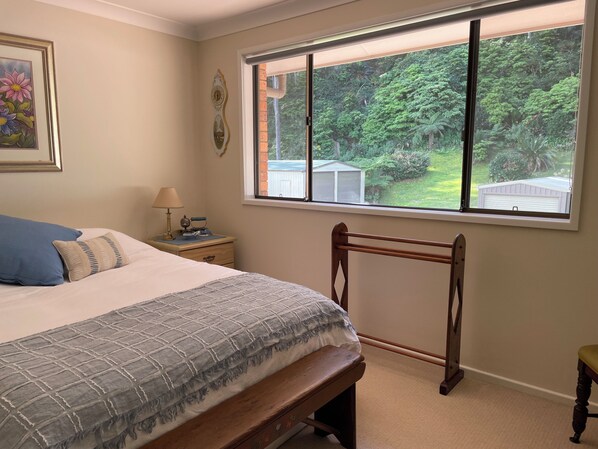 Ein Schlafzimmer mit großem Fenster, einem Bett mit grau-weiß gestreifter Bettdecke, einem Holzstuhl und einem Nachttisch mit Lampe und einer kleinen Dekoration.