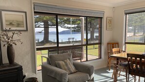 Un salon chaleureux avec une grande fenêtre donnant sur un magnifique lac et des montagnes. On y trouve un canapé confortable, une table à manger avec des chaises et une cheminée.