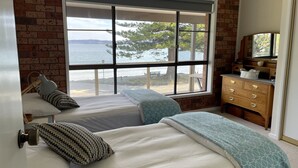 Une chambre avec deux lits, une commode et une grande fenêtre donnant sur la mer.
