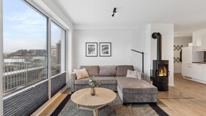 A modern living room with a large window, a sofa, a round coffee table, and a wood-burning stove. - GebirgsResort Winterberg (Winterberg)