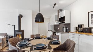 A modern kitchen with white cabinets, a black stove, and a dining area with a round table and brown chairs. - GebirgsResort Winterberg (Winterberg)
