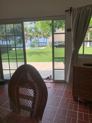 Une pièce dotée d’une grande porte-fenêtre coulissante donnant sur une piscine, d’un fauteuil en osier et d’un meuble en bois.