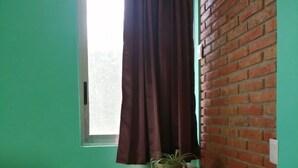 Een kamer met turquoise wanden, een raam met gordijn, een bakstenen muur, een houten bankje en een potplant op een houten tafel.