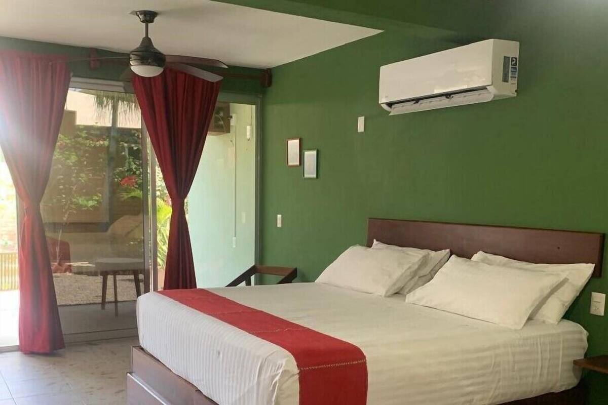 Ein Schlafzimmer mit einem großen Bett, einem Deckenventilator, einer Klimaanlage und Blick ins Freie durch eine Glastür.