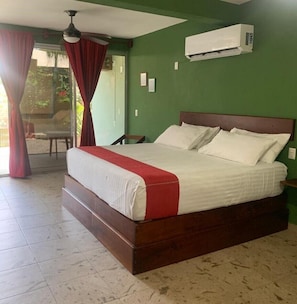 Ein Schlafzimmer mit einem großen Bett, einem Deckenventilator, einer Klimaanlage und Blick ins Freie durch eine Glastür.