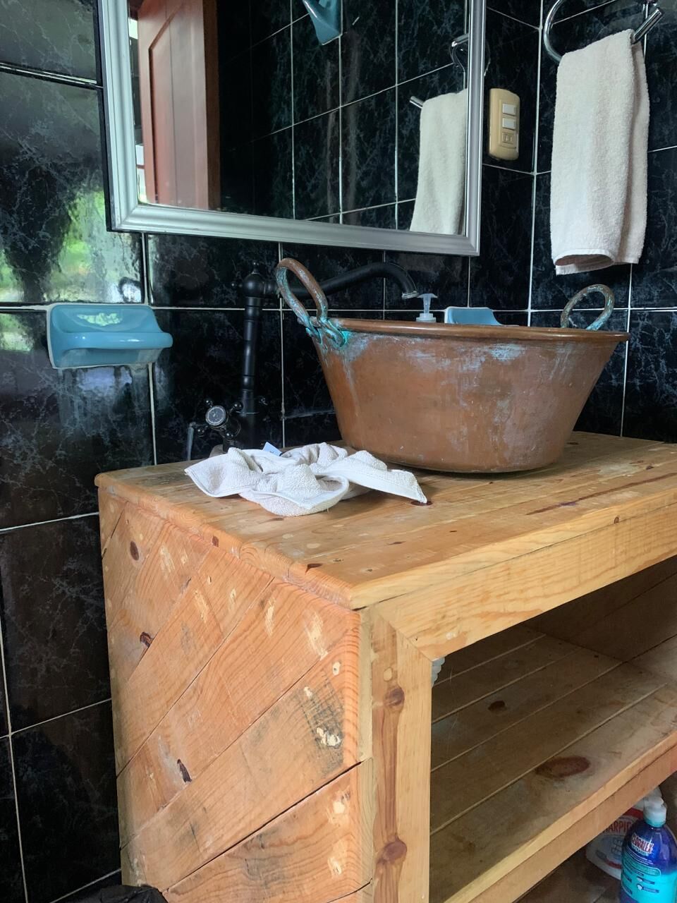 A wooden vanity with a large ceramic basin, a mirror, and a towel rack.
