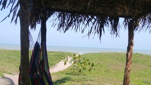 Een strandgedeelte met een rieten constructie, een hangmat, een houten bank en een kleine tafel.