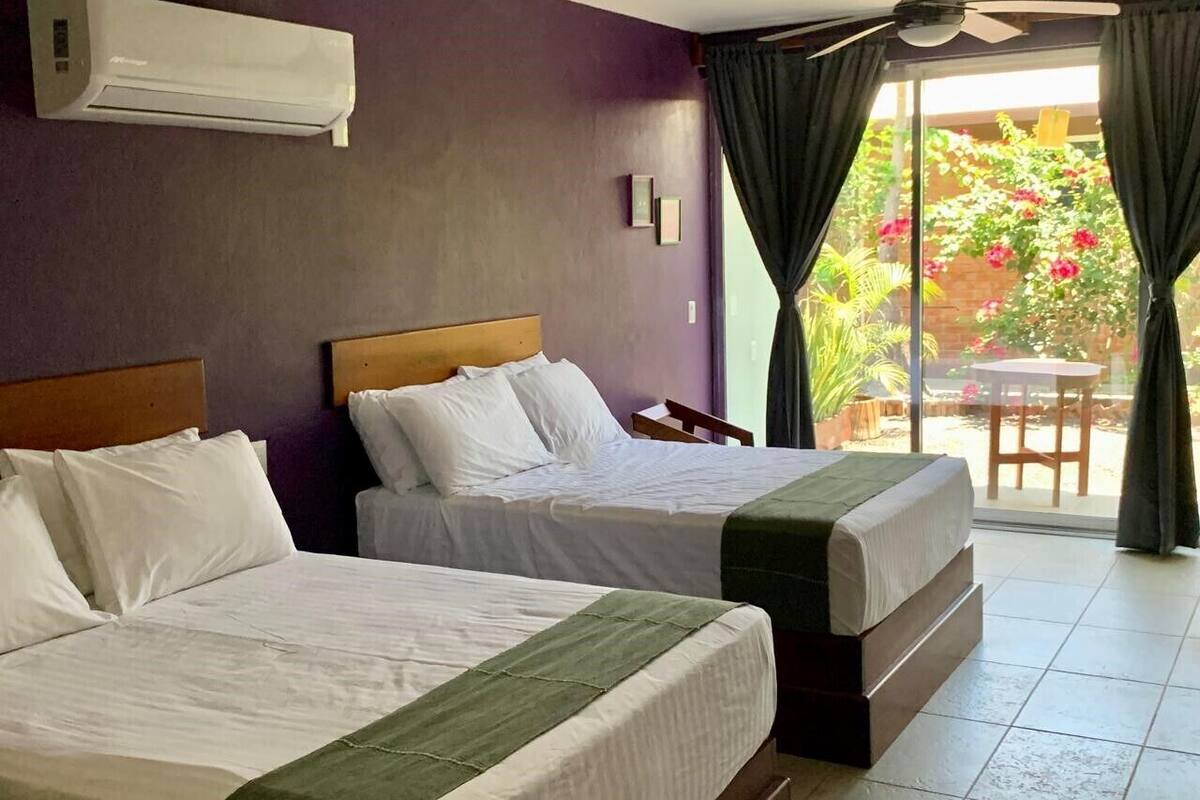 Ein Hotelzimmer mit zwei Betten, einem Deckenventilator und Blick auf einen Garten durch das Fenster.