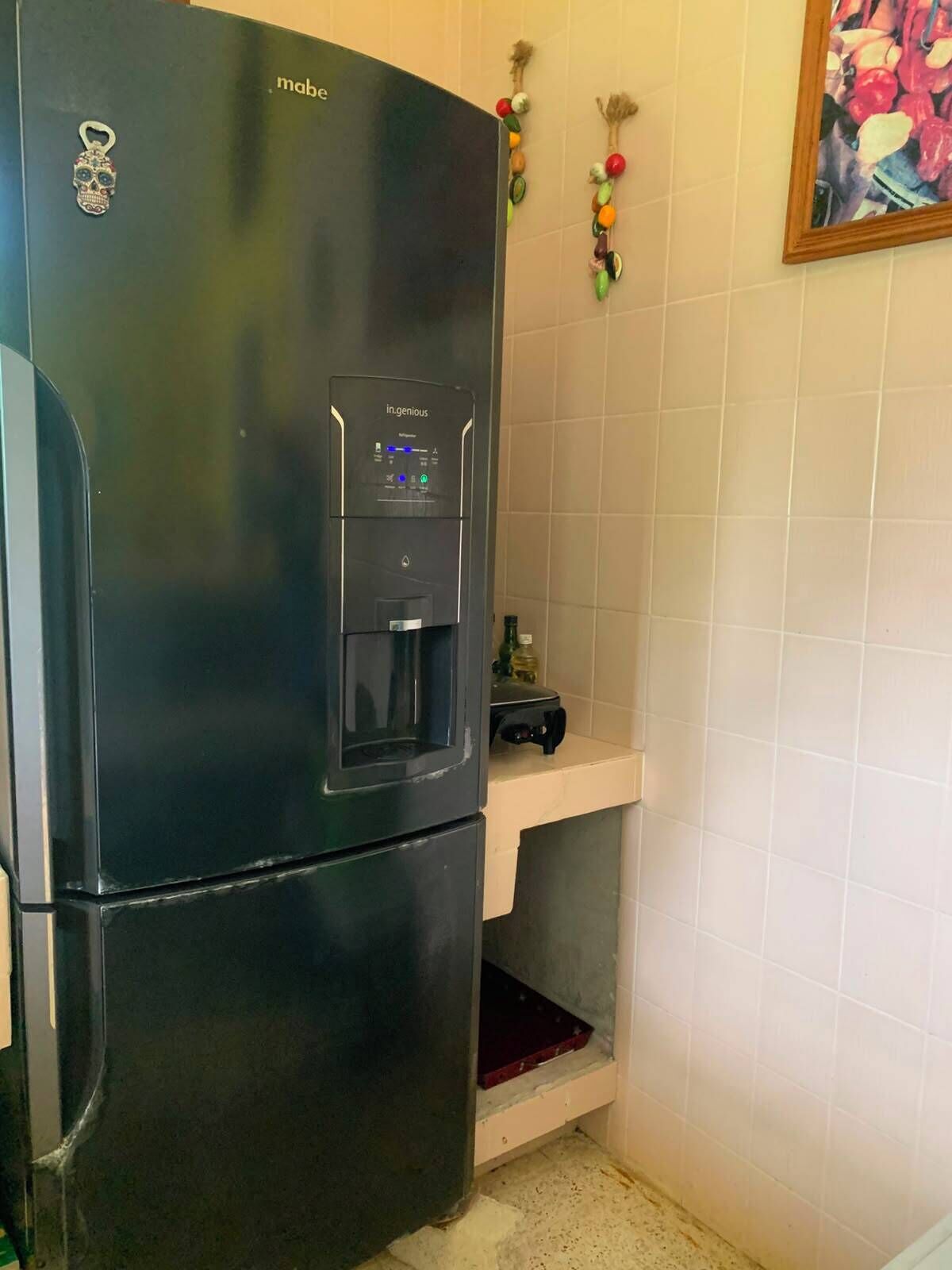 A black refrigerator with a water dispenser, a small shelf, and a bottle on top.