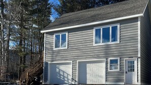 Ett tvåvåningshus med ett garage, en veranda och en trappa som leder upp till entrén.