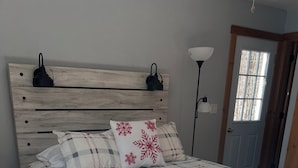 Ett sovrum med en sängram i trä, ett rutigt sängöverkast och ett nattduksbord.
