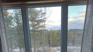 Ett rum med ett runt bord och två bekväma fåtöljer, stora fönster med utsikt över ett snötäckt landskap och träd.