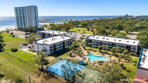 A hotel with multiple buildings, a large pool, and a view of the ocean.