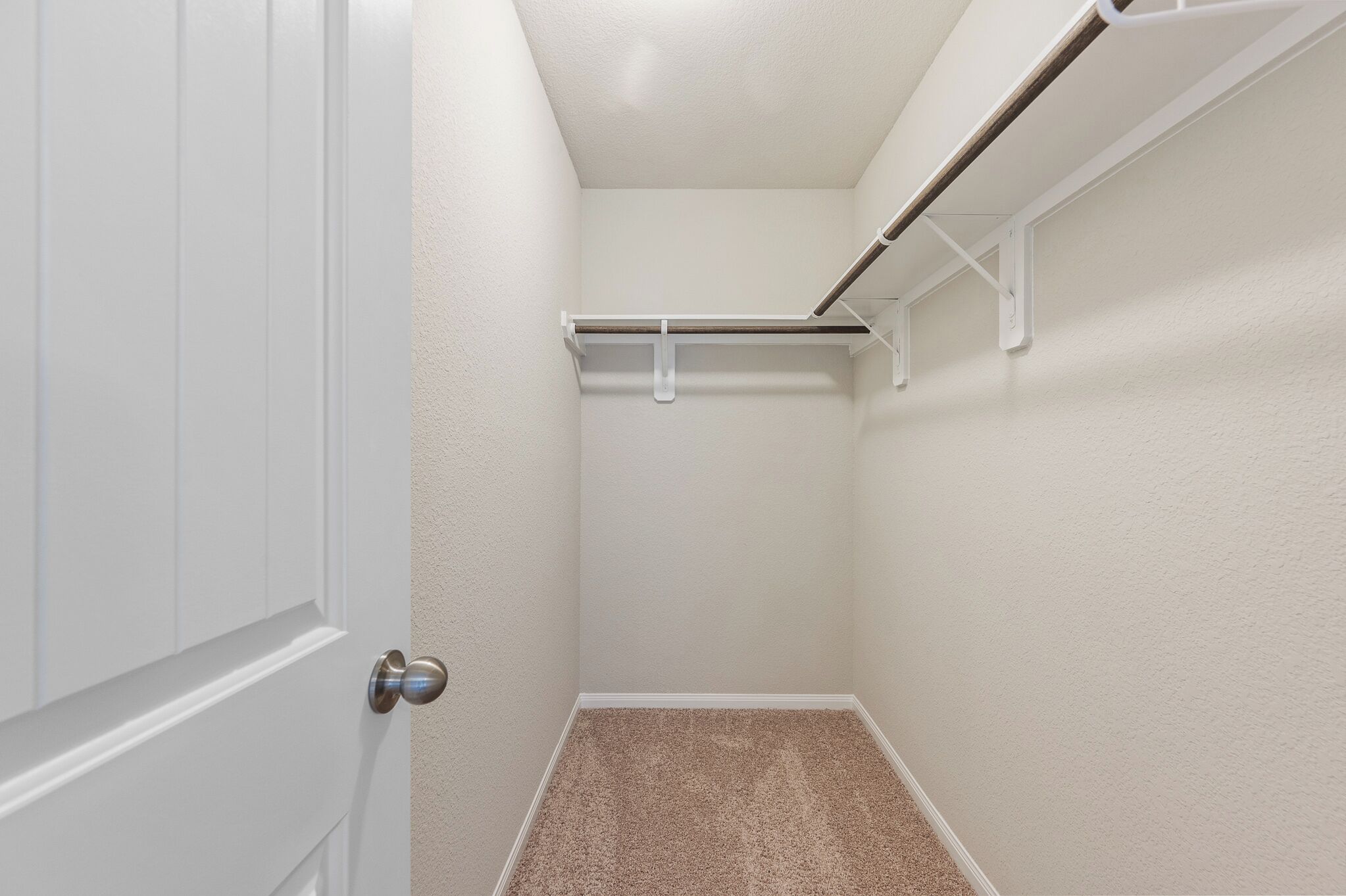 Un angolo di una stanza con una porta bianca, un tappeto beige e un soffitto bianco con un lampadario.