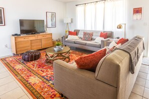 Una sala de estar con un sofá, una mesa de centro, un televisor y una alfombra estampada.
