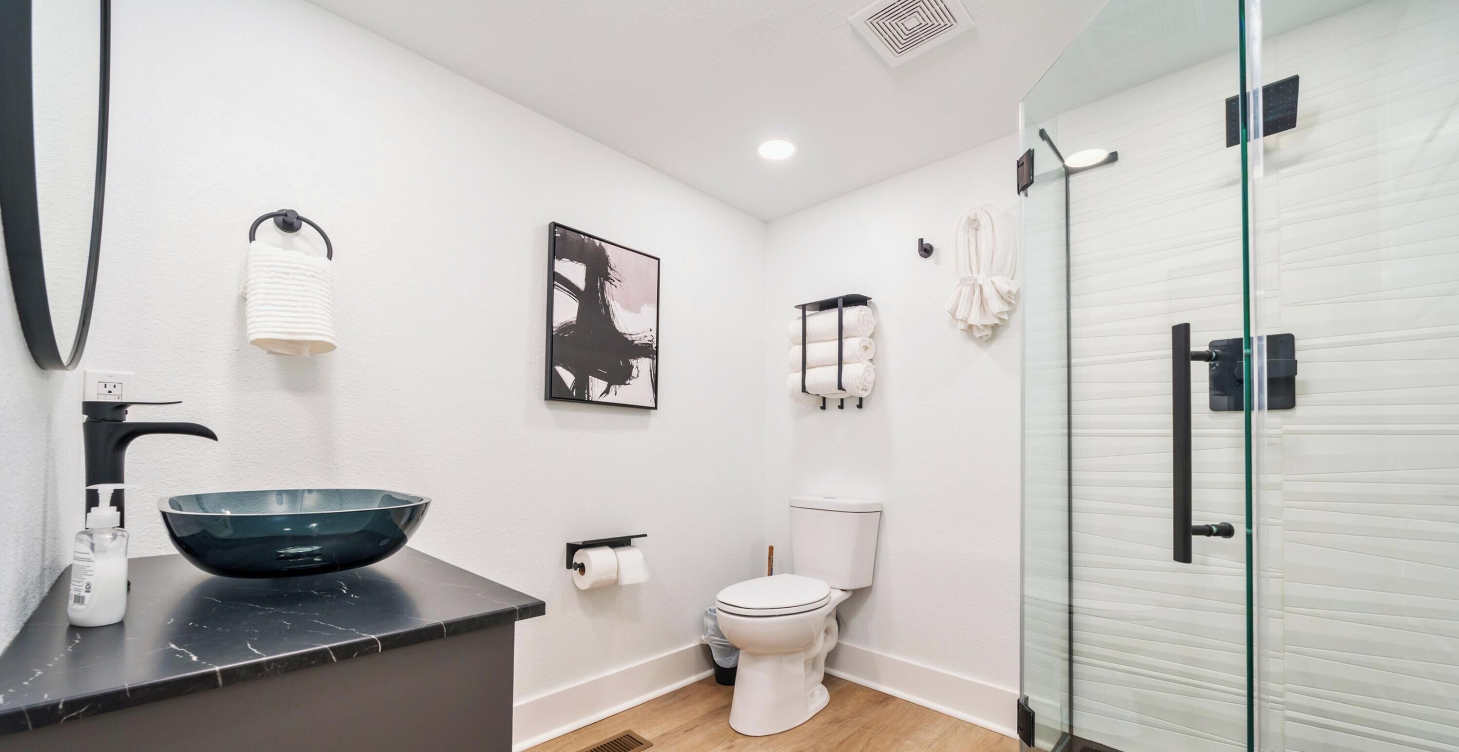A modern bathroom with a black marble sink, a glass shower enclosure, a toilet, and a wall-mounted towel rack.