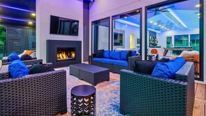 A modern outdoor lounge area with wicker furniture, a fireplace, and large windows. - Discover Lakeside Bliss on Lake Hamilton (Hot Springs)