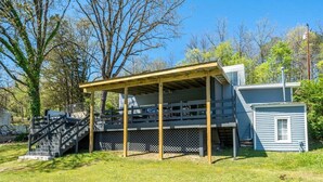 Un espacio al aire libre techado con una escalera que lleva a una terraza, rodeado de árboles y una casa.
