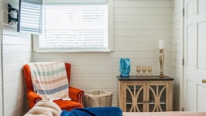 Una habitación con una cama, una silla, una mesita con lámpara, una ventana con persianas y una puerta.
