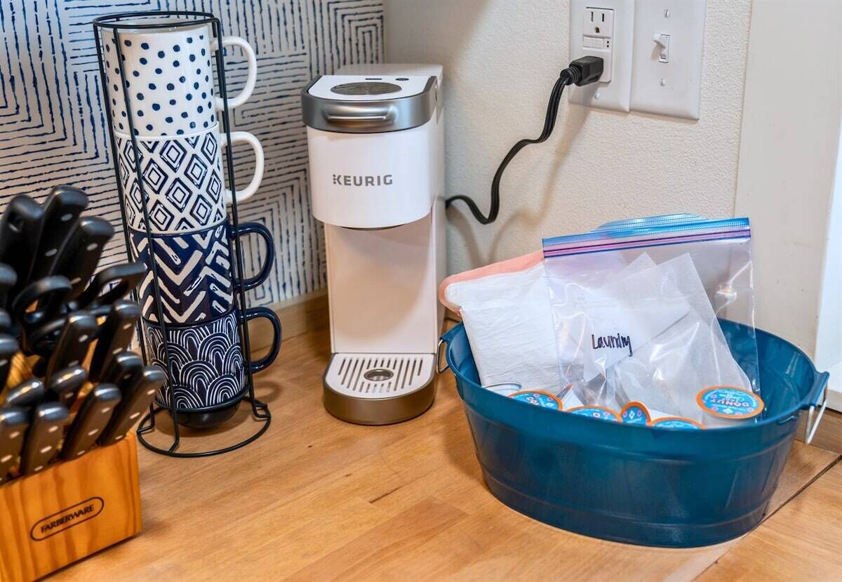 A kitchen area with a coffee maker, a mug, a knife holder, and a trash bin.