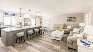 Eine moderne Küche mit einer zentralen Kochinsel, Barhocker und einem Essbereich mit weißem Tisch und Stühlen.