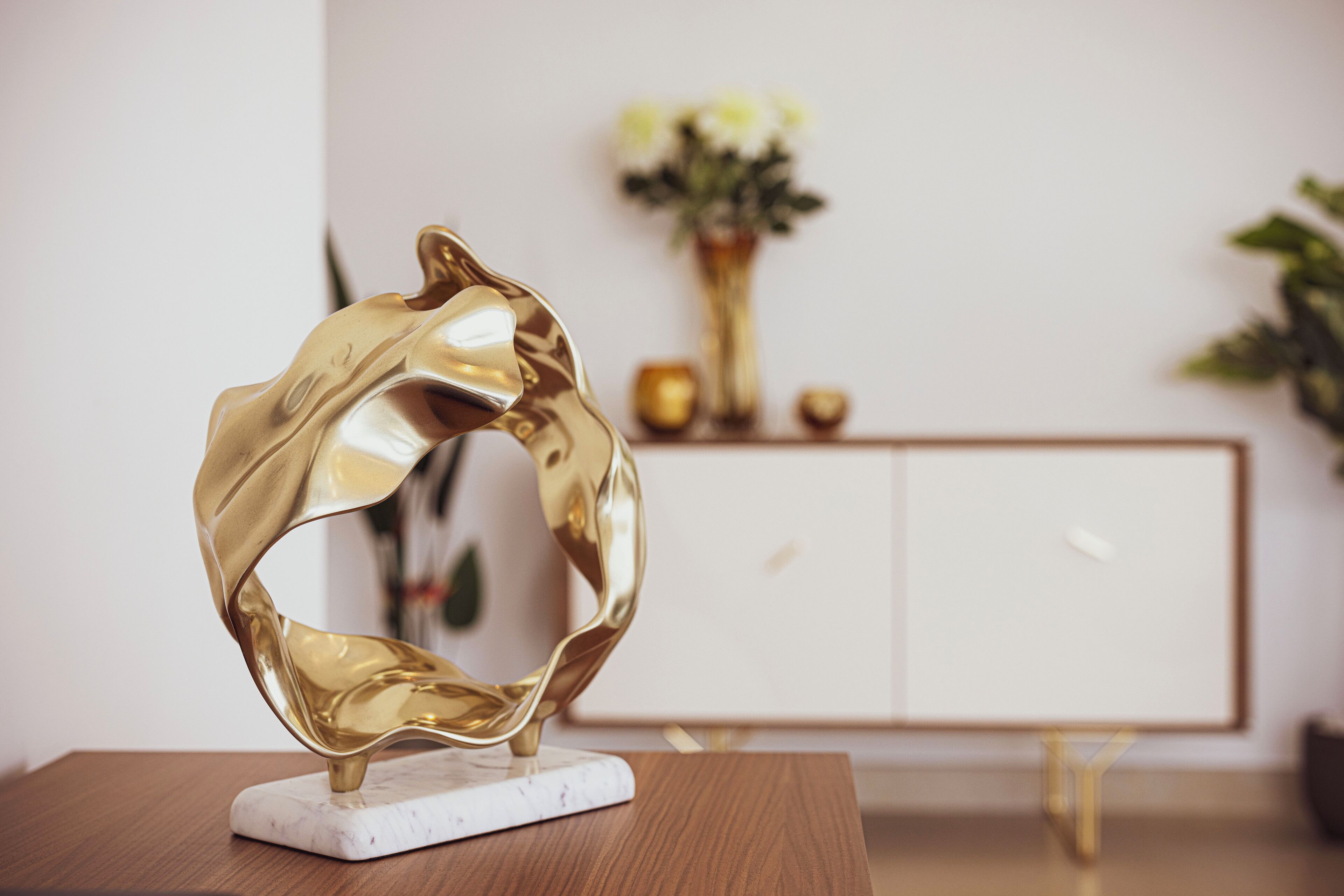 Eine goldene, abstrakte Skulptur auf einem Marmorsockel.