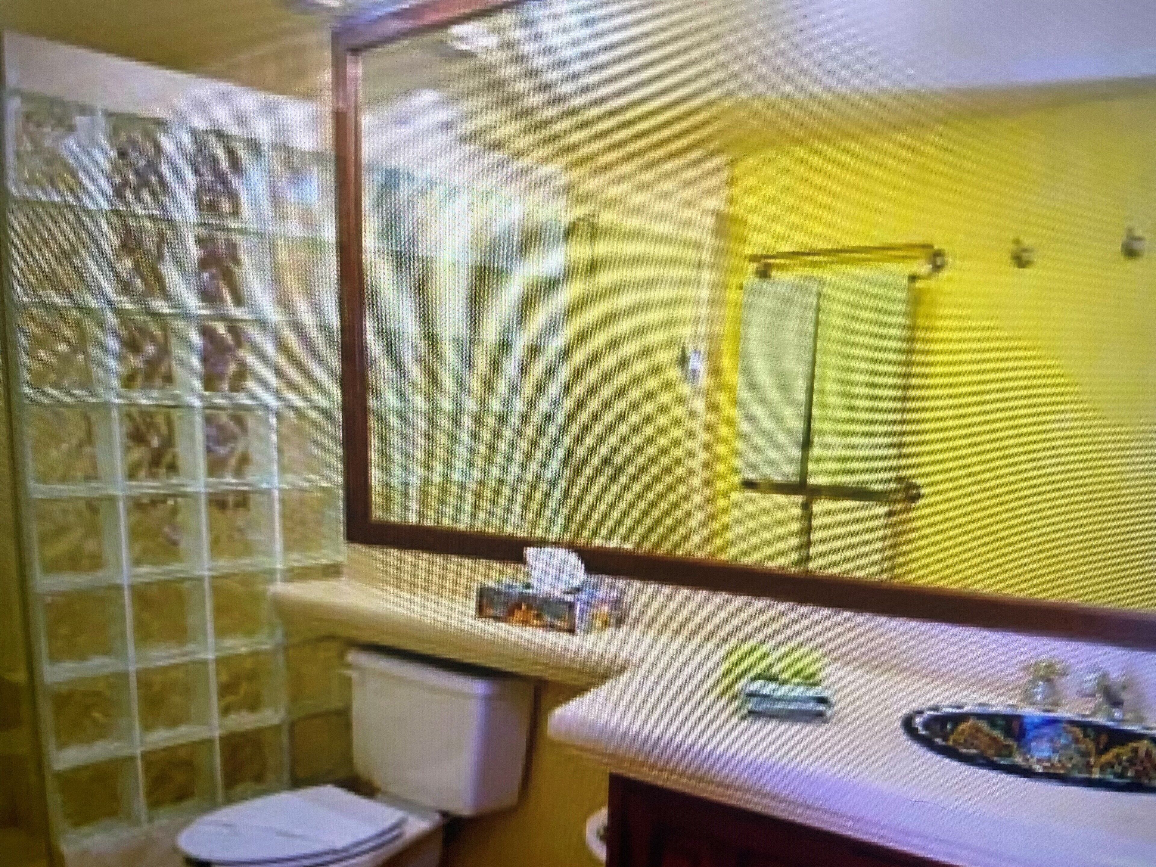 Un baño con inodoro, lavamanos y espejo, con una toalla amarilla colgada en la pared.