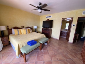 A hotel room with a bed, a bench, a TV, and a ceiling fan. - Luxurious beachfront condo on Riviera Maya, 2 bdrm, large balconies, 1575 sq ft (Puerto Aventuras)