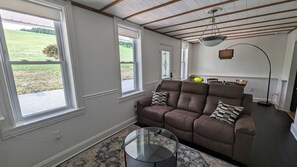 Een woonkamer met een bruine leren bank, een glazen salontafel en uitzicht op een groen veld door grote ramen.