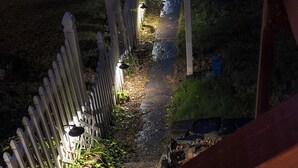 Ett trädäck med en gång av sten som leder fram till en grindad entré.