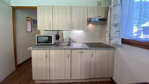 Cocina compacta con armarios de madera clara, microondas integrado y ventana con vistas al exterior.