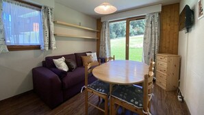 Una habitación acogedora con una mesa redonda de madera, un sofá púrpura y un armario de madera.
