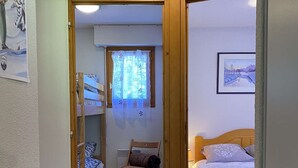 Una habitación pequeña y acogedora con una cama nido, una cama individual, una silla y una ventana con vistas.