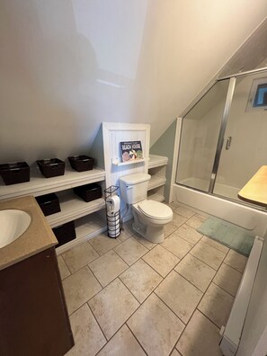 Een badkamer met een toilet, een wastafel, een douche en planken met manden.