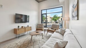 Een moderne woonkamer met een groot raam, een flatscreen televisie, een bank, een salontafel en een dressoir.