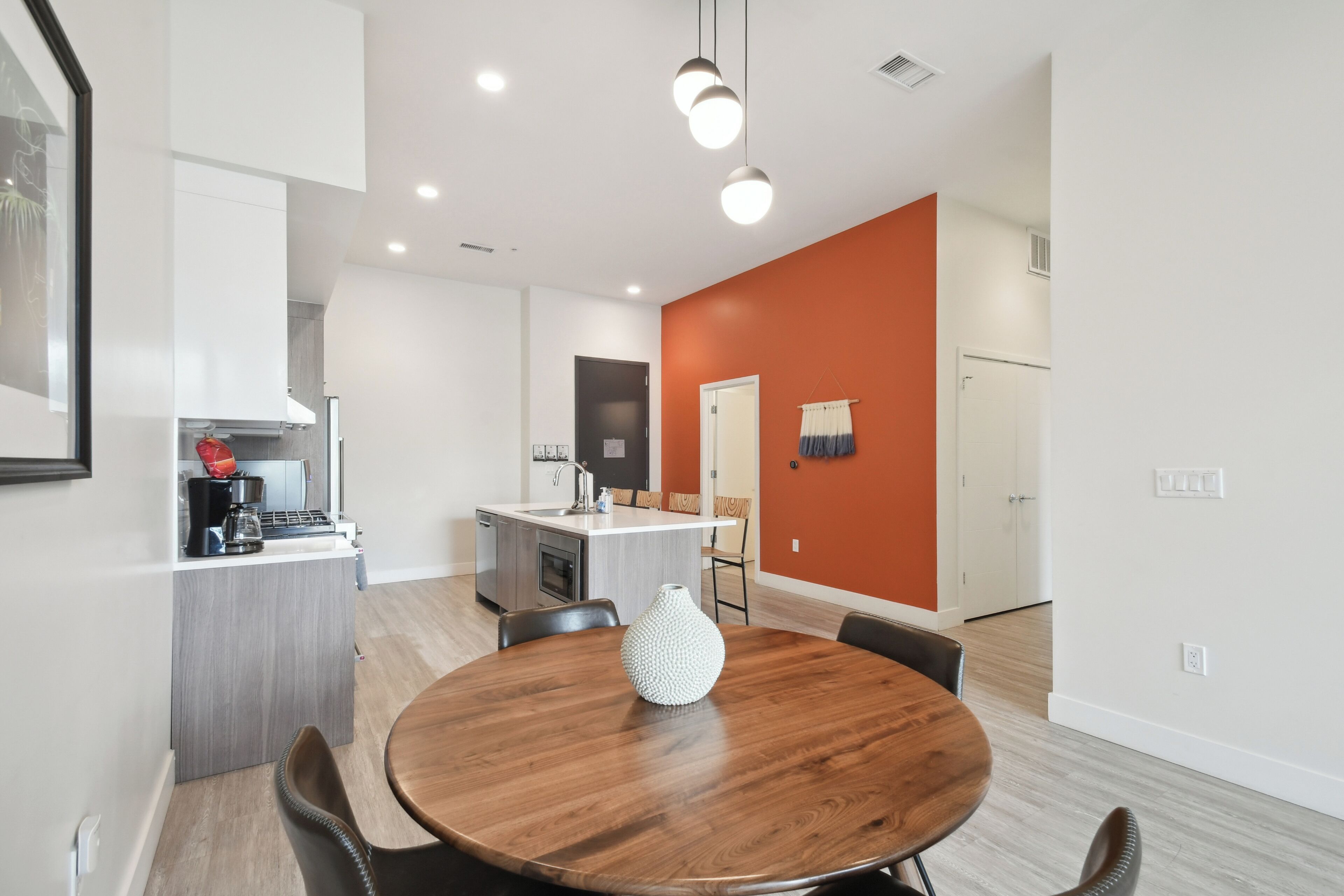 A modern kitchen with a built-in island, a dining area with a wooden table, and a bright orange accent wall.