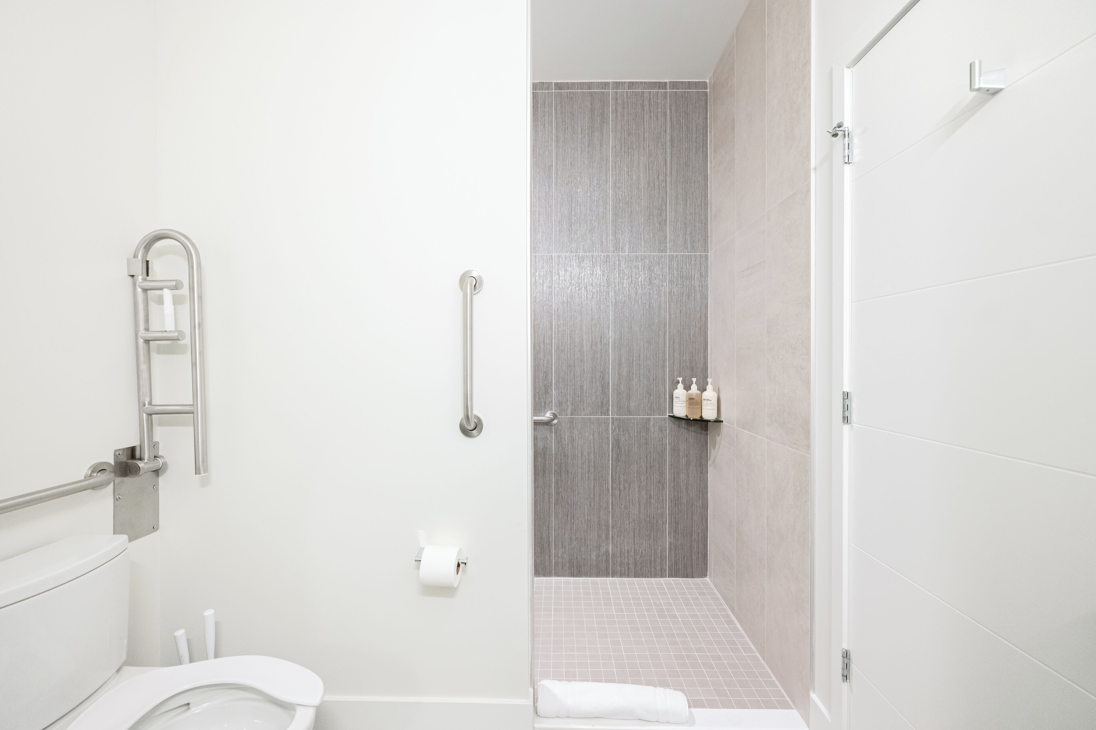 A modern bathroom with a toilet, a shower with a glass door, and a handrail.