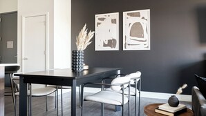 Un espace repas moderne avec une table noire, des chaises blanches et un vase contenant des plantes séchées. Deux œuvres d’art abstraites sont accrochées au mur.