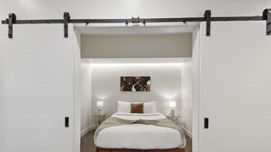 A bedroom with a wooden bed, white walls, a black ceiling track, and a painting on the wall.