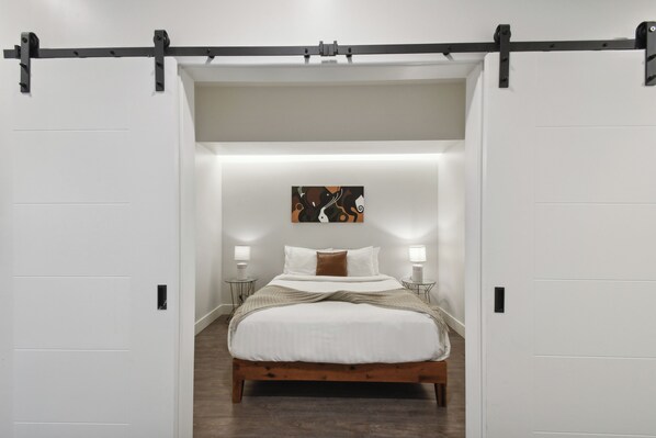 Une chambre à coucher avec un lit en bois, des murs blancs, un rail noir au plafond et un tableau accroché au mur.