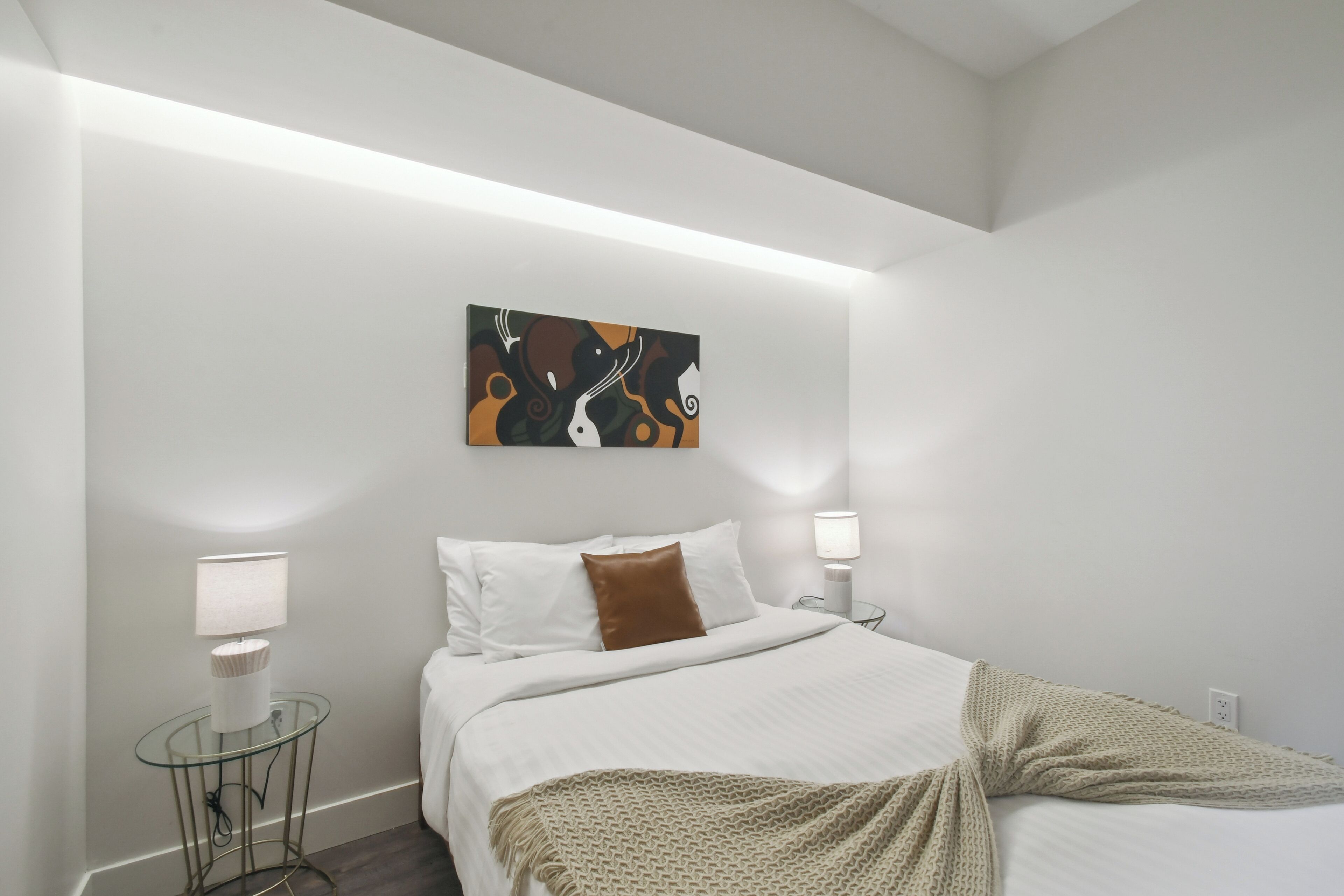 Een moderne slaapkamer met een bed, witte muren, een schilderij en twee bedlampen.