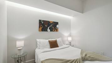 Een moderne slaapkamer met een bed, witte muren, een schilderij en twee bedlampen.