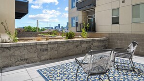 A rooftop patio with two metal chairs, a patterned rug, and a view of the city skyline. - Art Inspired Stay | 1BR LoHi Loft | Dog-Friendly (Denver)