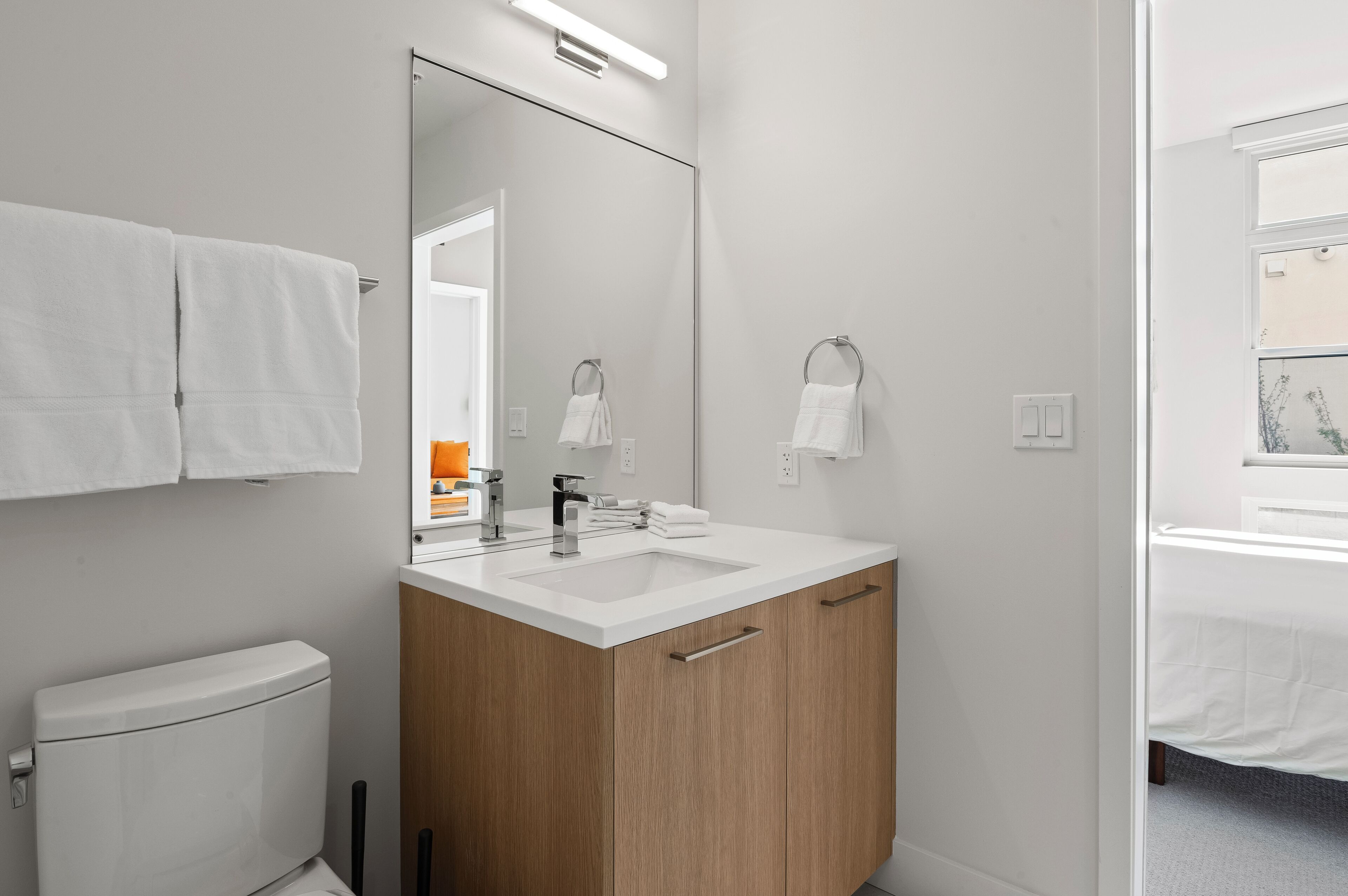 A modern bathroom with a white sink, wooden vanity, and a large mirror.