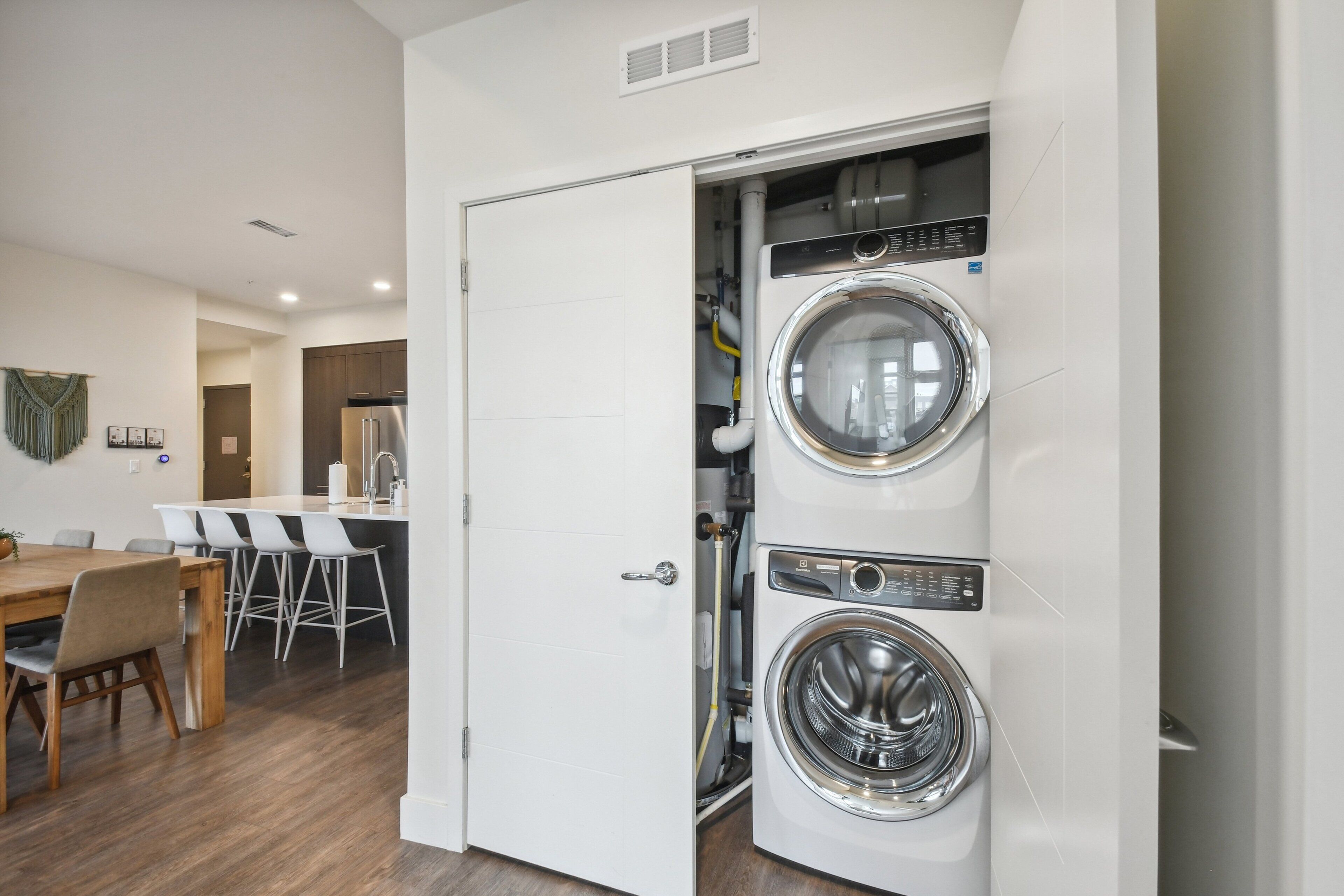 A laundry room with two front-loading washing machines, a dining area with a table and chairs, and a kitchenette with a refrigerator.