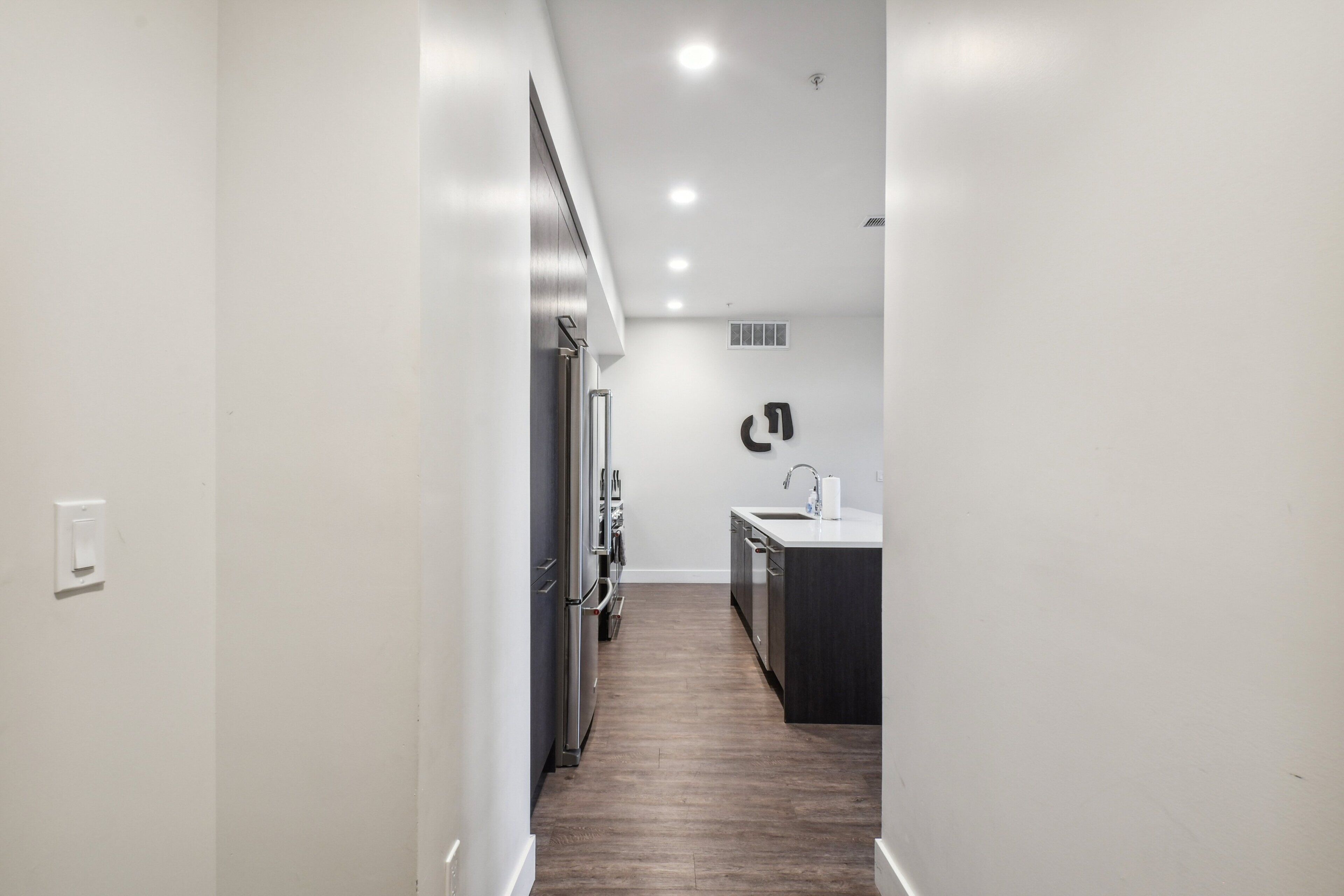 A narrow hallway leading to a kitchen with a sink and cabinets.