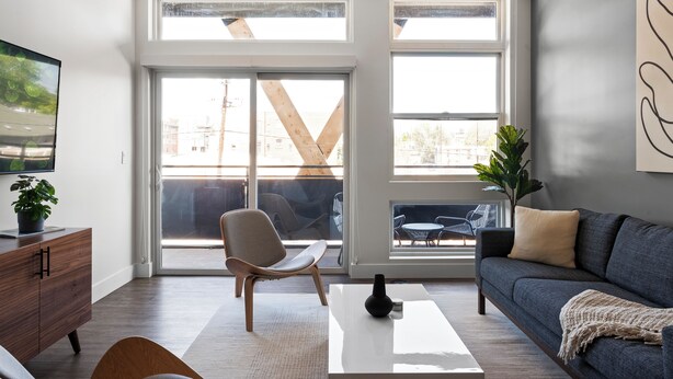 Ein modernes Wohnzimmer mit Sofa, Couchtisch und Sessel. Ein großes Fenster bietet einen Ausblick nach draußen.