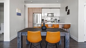 Eine moderne Küche mit Edelstahlgeräten, einem Essbereich mit einem dunklen Holztisch und orangenen Stühlen sowie einer Pendelleuchte.