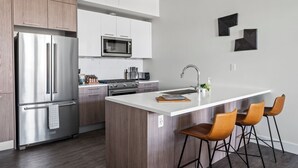 Eine moderne Küche mit Edelstahlgeräten, Holzschränken, einer weißen Kücheninsel mit Barhocker und einer Mikrowelle über dem Herd.